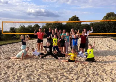 Eine Gruppe von Sportlern posiert auf einem Sandplatz, umgeben von Bäumen und einem Netz.